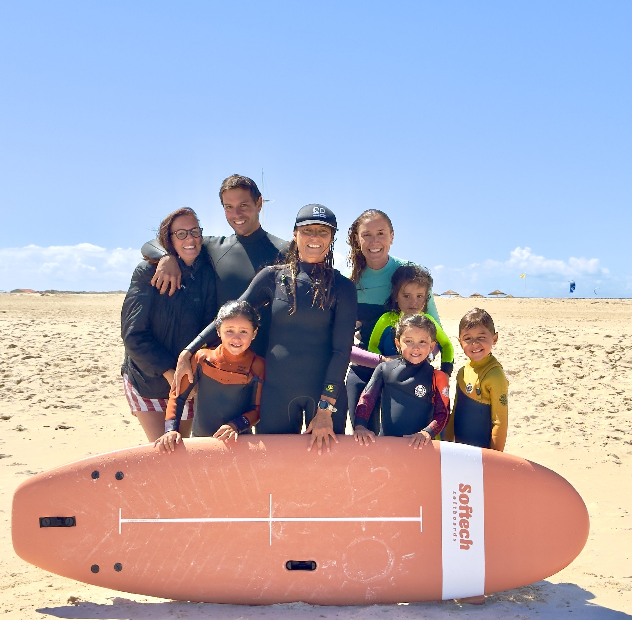 Grupo de adultos e crianças com uma prancha na praia, na Good Surf Good Love.