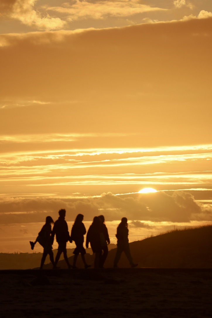 Grupo a caminhar junto ao mar, ao pôr do sol